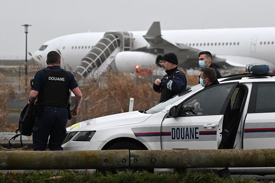 Los agentes de aduanas franceses se encuentran junto a un vehículo de aduanas con un Airbus A340 al fondo que estuvo parado desde el 21 de diciembre en la pista por sospecha de "tráfico de personas", en el aeropuerto de Vatry, Francia. Foto: AFP/ NI