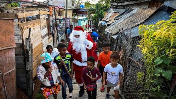 Un hombre vestido de Papá Noel camina con niños por las calles de La Habana el 21 de diciembre de 2023. Foto: Yamil LAGE / AFP.